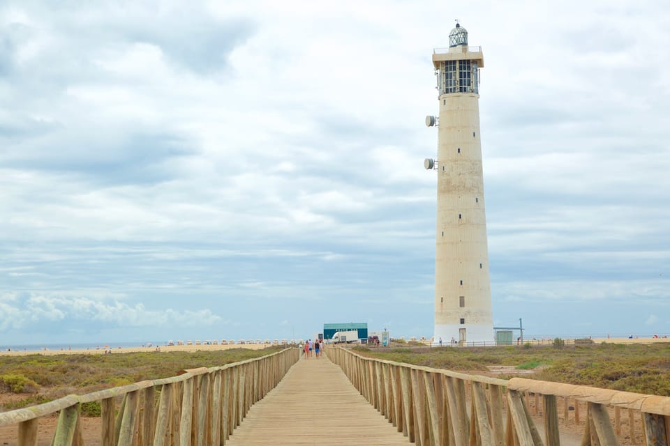 Una pasarela de madera que lleva a un alto faro con veleta en la parte superior.