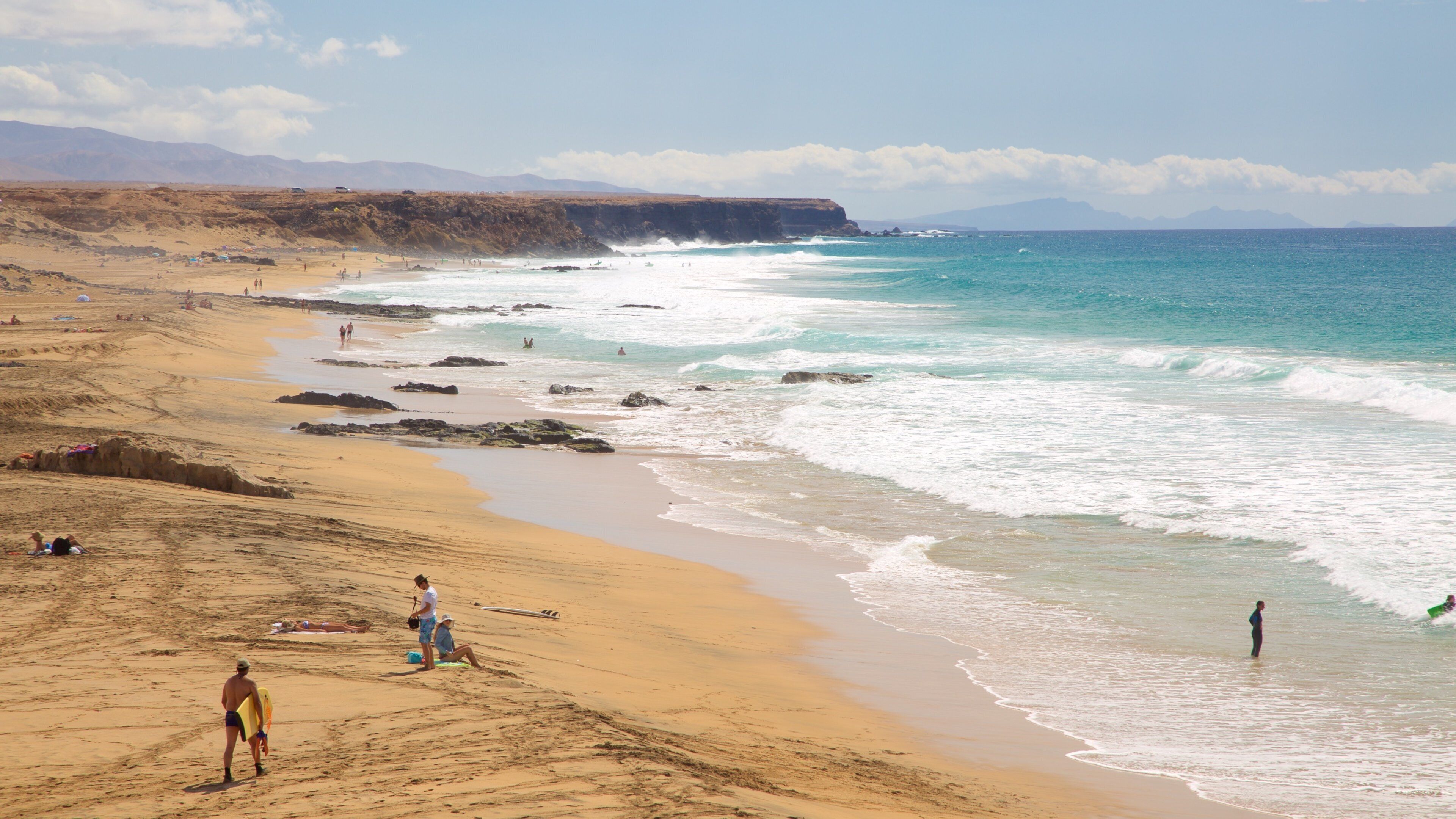 A beach with people, waves, and distant mountains.