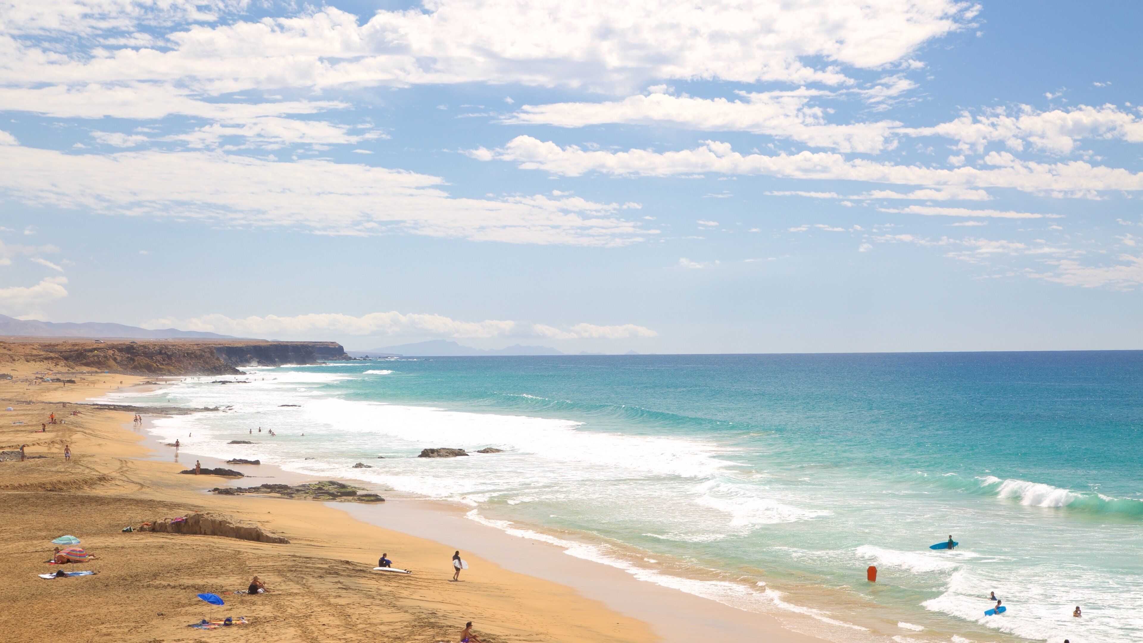 A beach with clear turquoise waters, sandy shore, and rocky cliffs in the background.