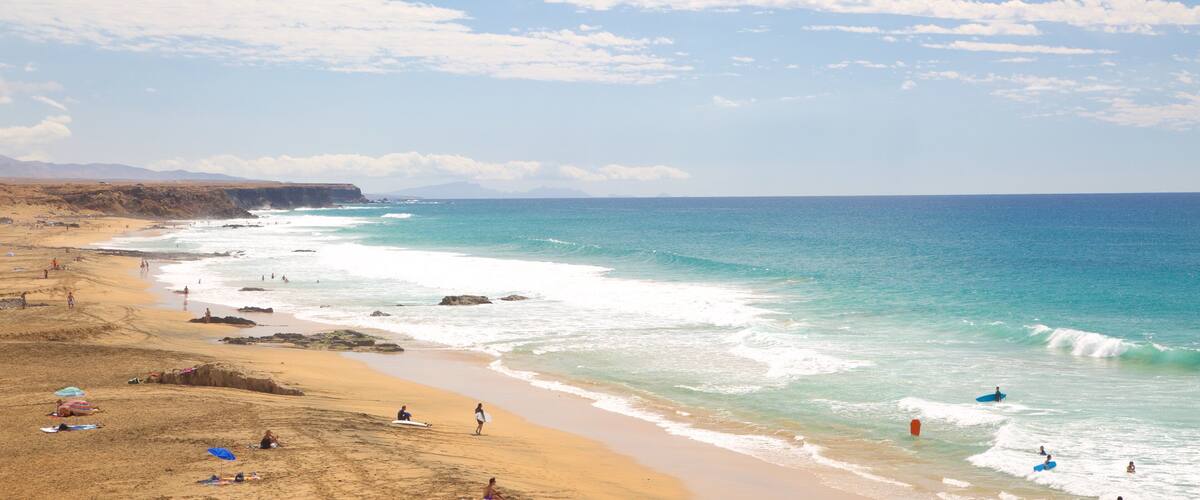 A beach with clear turquoise waters, sandy shore, and rocky cliffs in the background.