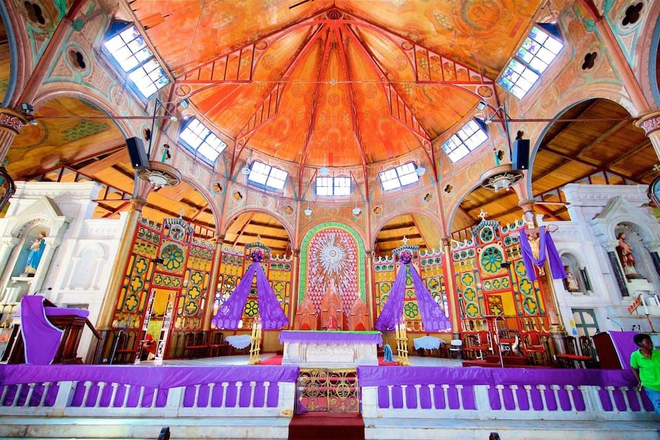 L’intérieur d’une église, avec un plafond richement décoré et aux couleurs vives, des vitraux et un autel central.