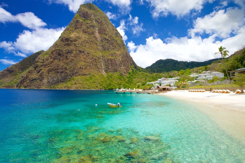 Une plage tropicale aux eaux turquoise et limpides, une grande montagne conique et une zone touristique avec des bungalows.
