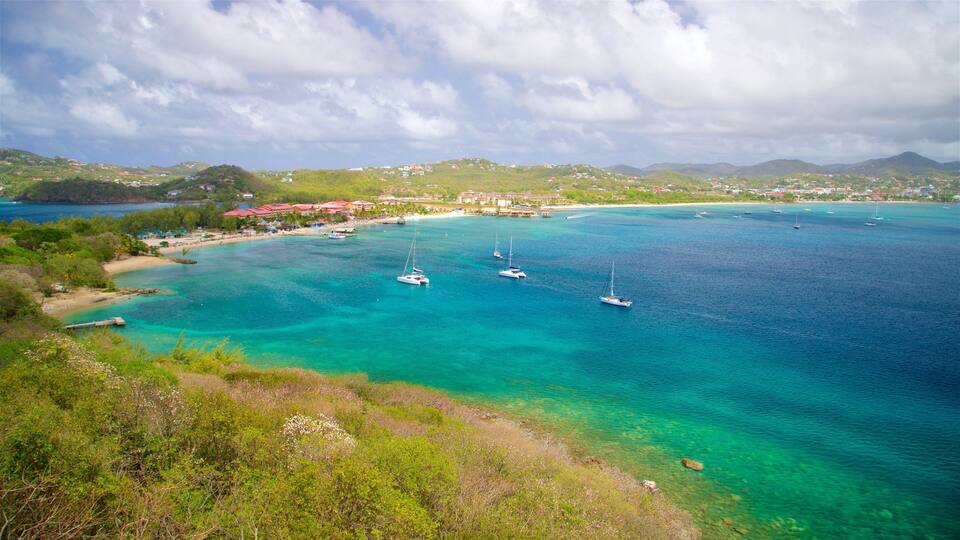 A coastal town with clear turquoise waters, several sailboats, and a backdrop of green hills and mountains.