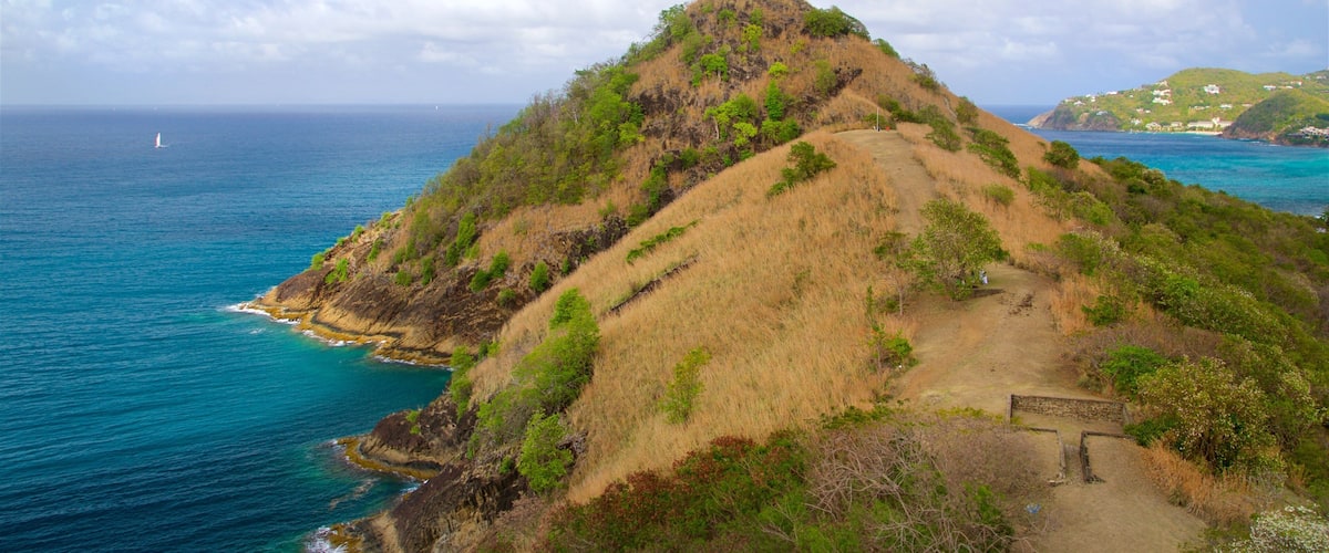 A coastal landscape with a prominent hill, a clear view of the ocean, and a distant shoreline with buildings.