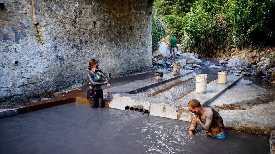 A stone structure with a water basin, a person in the water, and another person standing nearby.