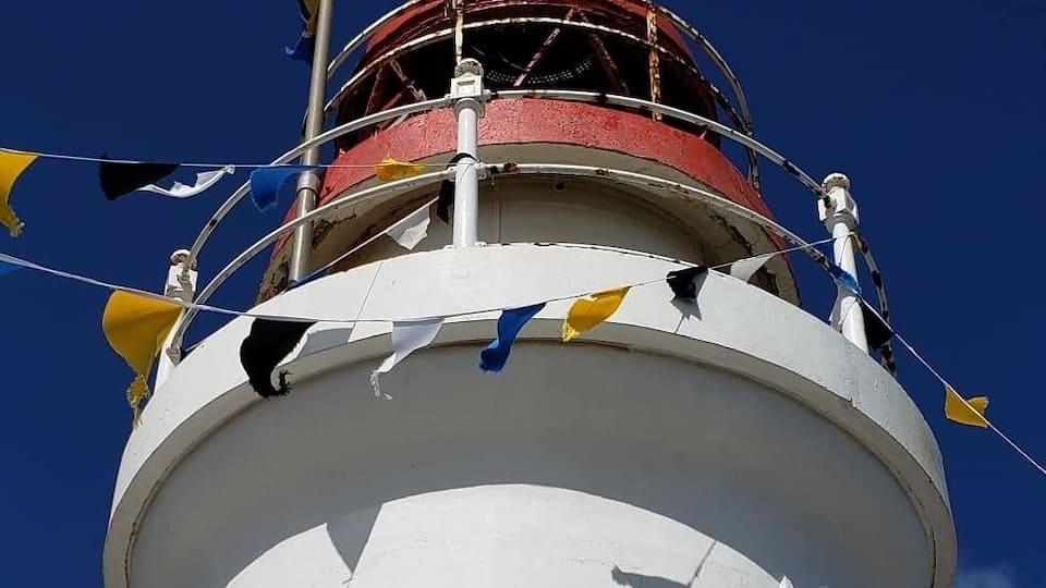 A lighthouse with a red top and white base, adorned with colorful flags.