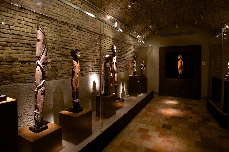 A museum corridor with wooden sculptures on display against a brick wall.