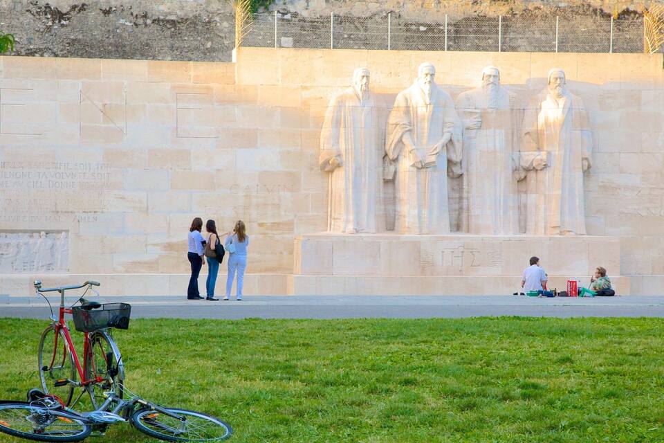 A monument with statues and inscriptions, a bicycle, and people in the foreground.
