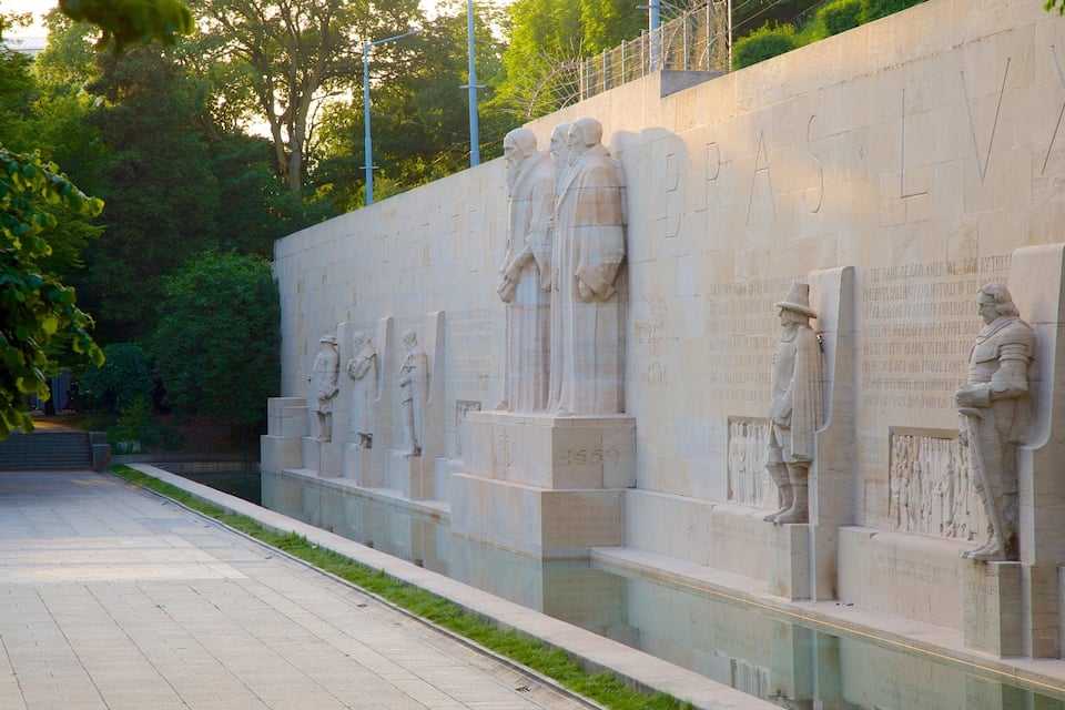 A series of statues on a wall with inscriptions, a paved walkway, and greenery in the background.