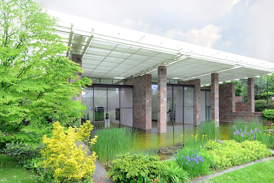 A modern building with a glass facade, surrounded by lush greenery and a small pond.