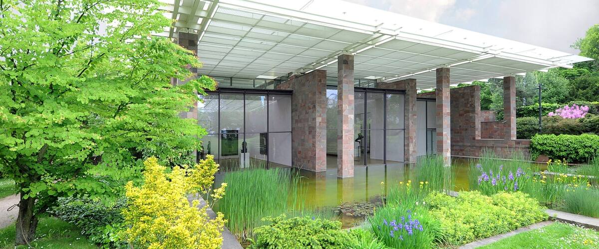 A modern building with a glass facade, surrounded by lush greenery and a small pond.