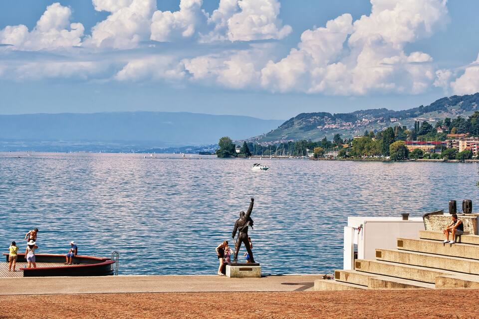 A lake with a statue, people on a dock, and a boat in the distance.