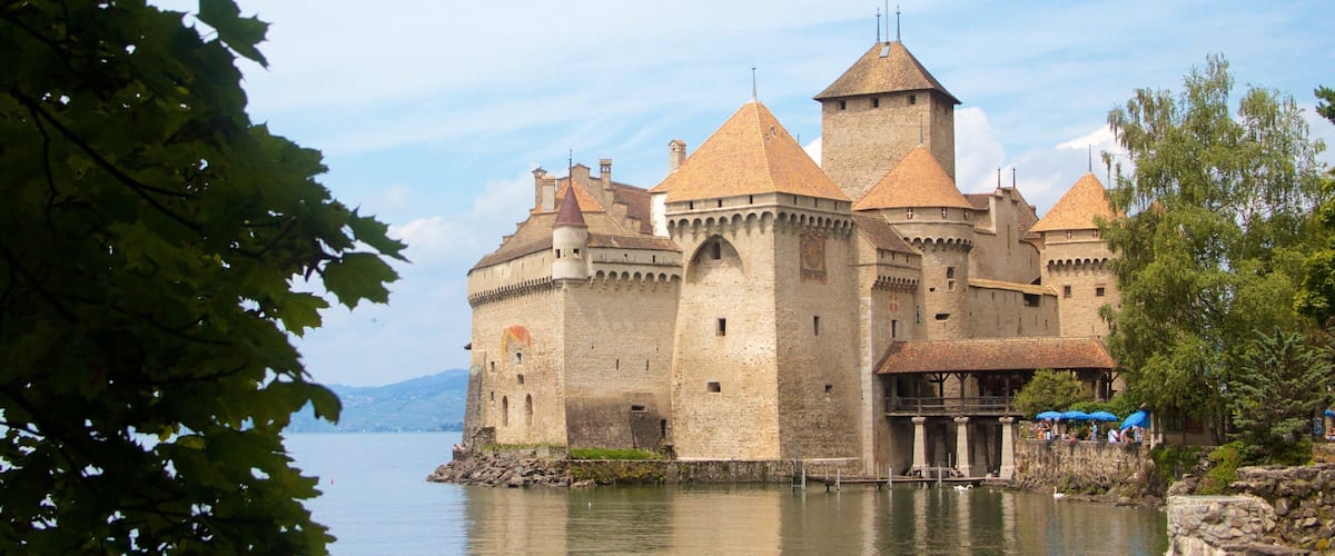 Eine historische Burg an einem See, mit mehreren Türmen und einer roten Flagge auf dem Dach.