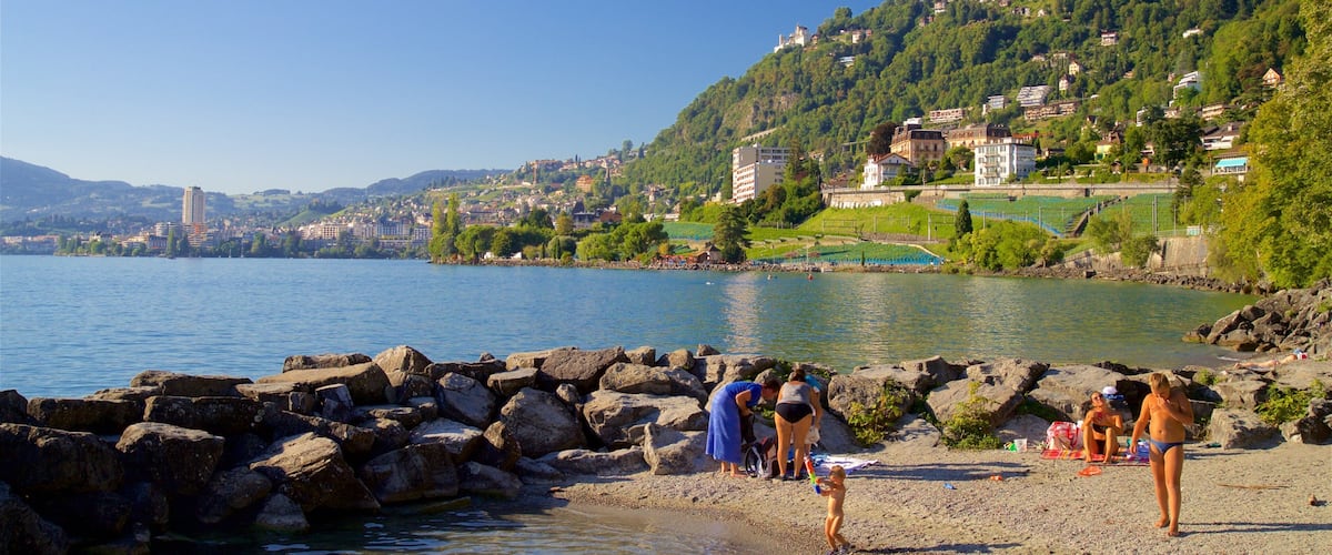 A lakeside town with rocky shores, people by the water, and buildings on a hillside.