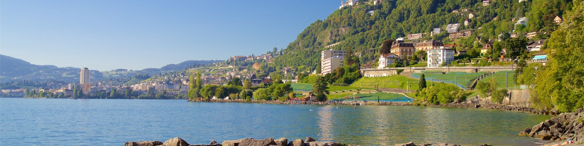 A lakeside town with rocky shores, people by the water, and buildings on a hillside.