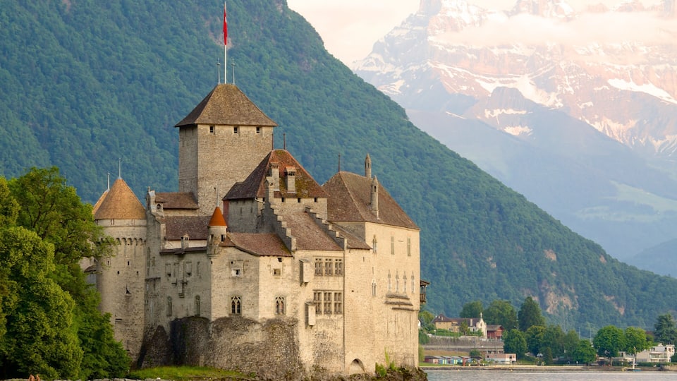 A historic castle with multiple towers, surrounded by lush green mountains and a river.