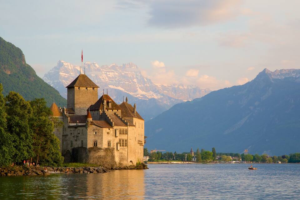 Un castillo junto a un lago, con montañas al fondo.