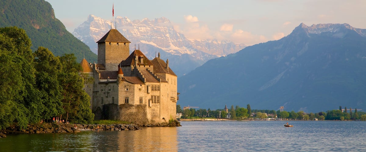 A castle by a lake with mountains in the background.