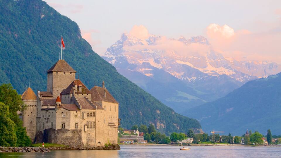 A historic castle by a lake with mountains in the background.
