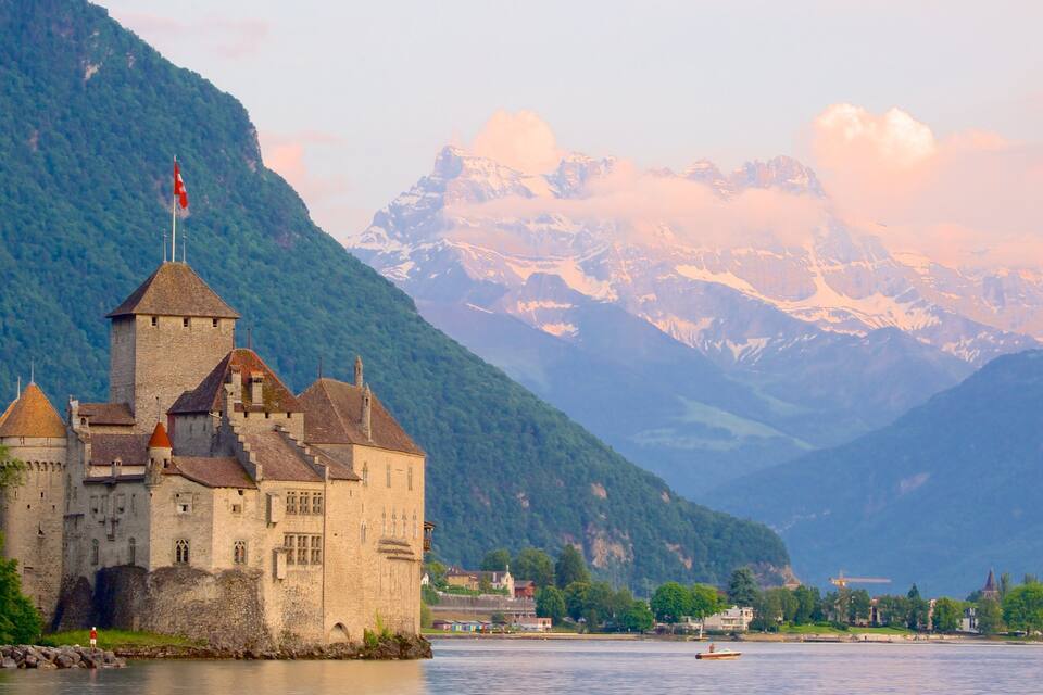 Un château historique situé au bord d’un lac, avec des montagnes en toile de fond.