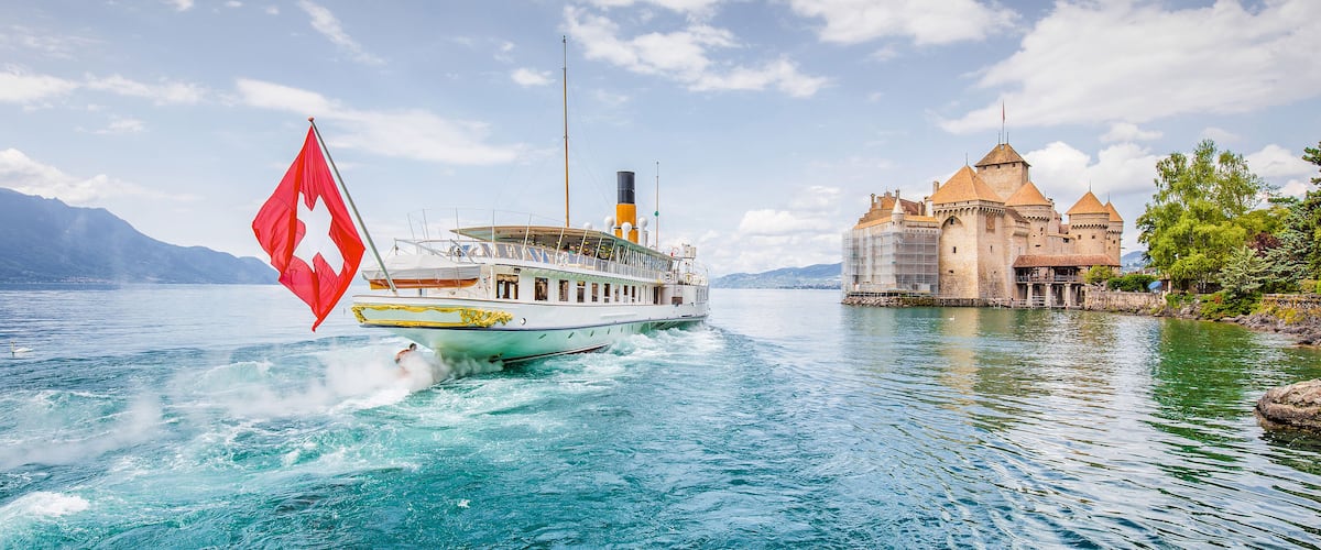 Scenic panorama view of traditional paddle steamer excursion ship with historic Chateau de Chillon at famous Lake Geneva on a sunny day with blue sky and clouds in summer, Canton of Vaud, Switzerland;