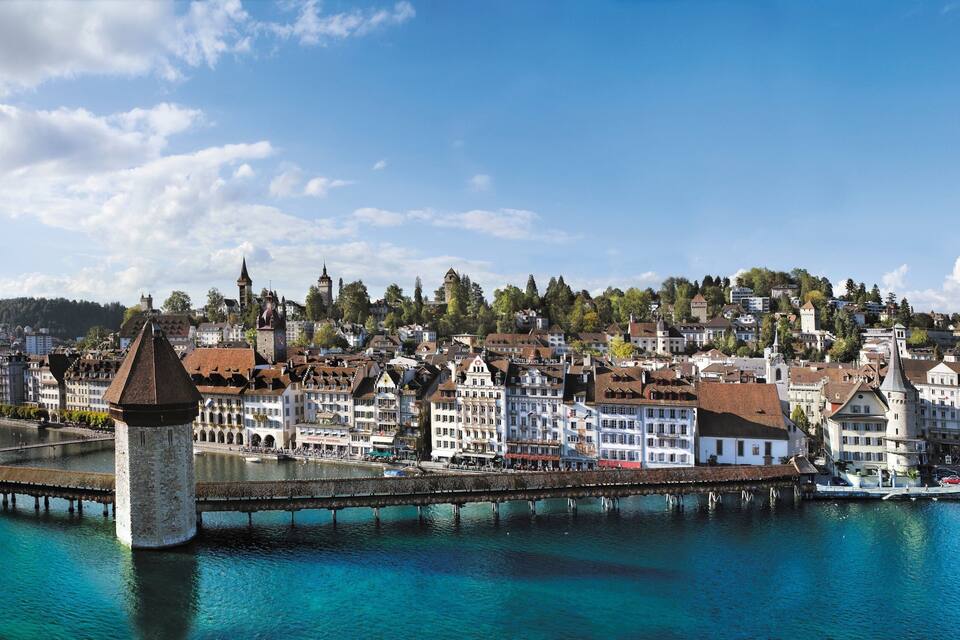 Une ville riveraine dotée de bâtiments historiques, d’un imposant beffroi et d’un pont enjambant le cours d’eau.