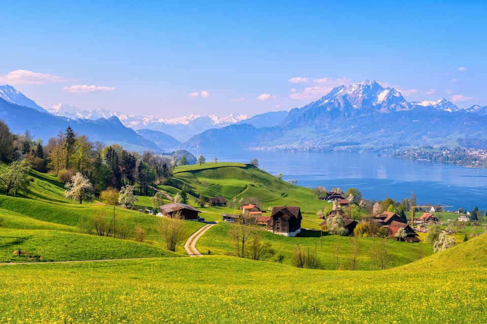 Un paisaje montañoso con un lago, campos verdes y casas tradicionales.