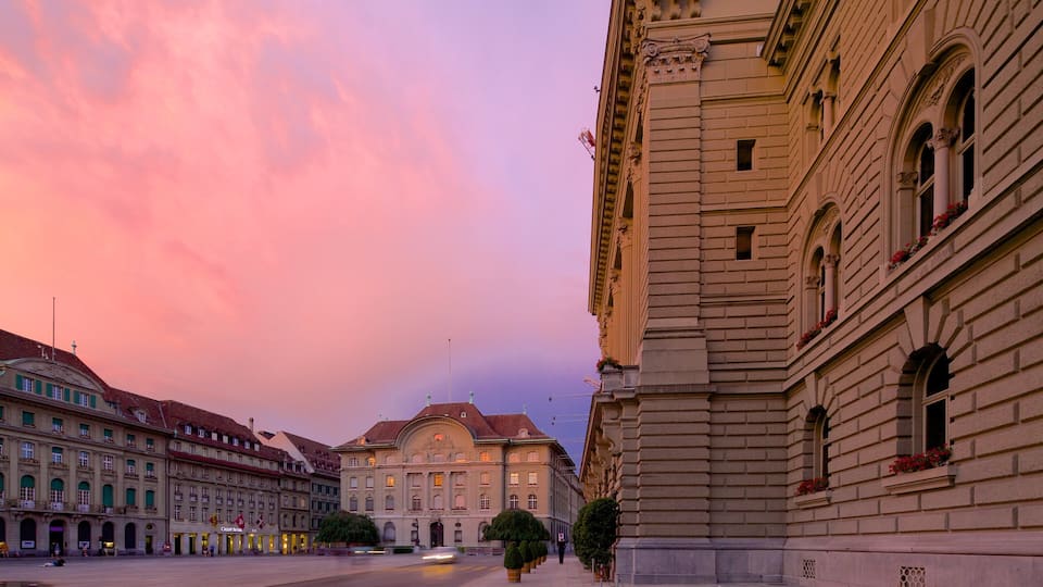 A historic building with ornate architecture, a large open square, and a pink sky.