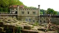 A historic building with a tower, surrounded by stone ruins and greenery.
