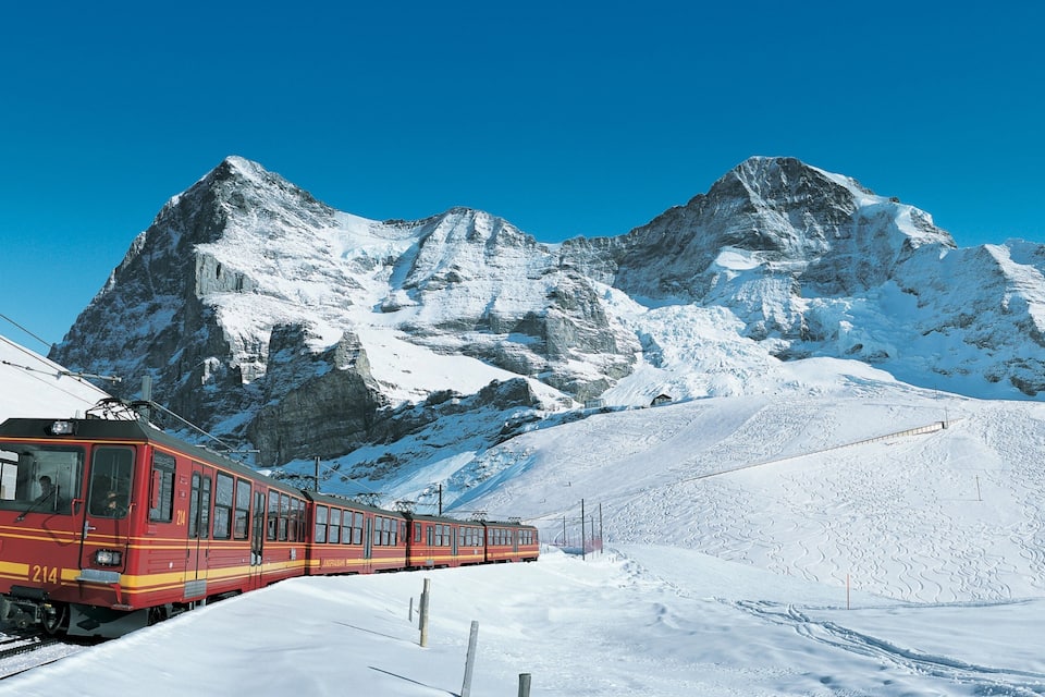 A red train on tracks in a snowy mountainous area.