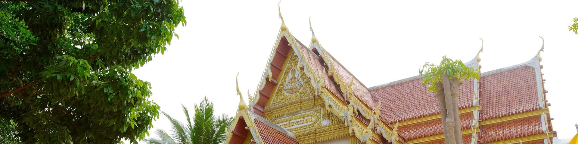 A traditional Thai temple with ornate architecture, red tiled roofs, and multiple flags.