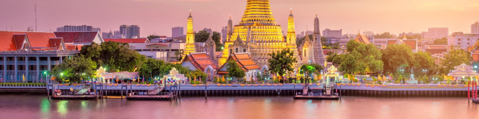 A golden pagoda with a reflection in calm water, surrounded by city buildings and trees.