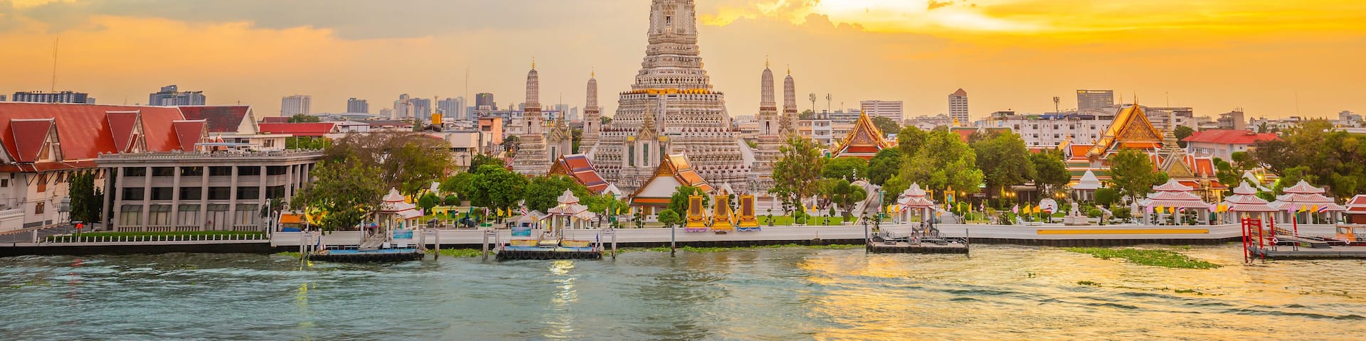 A cityscape with a prominent temple complex, a body of water, and a sunset sky.