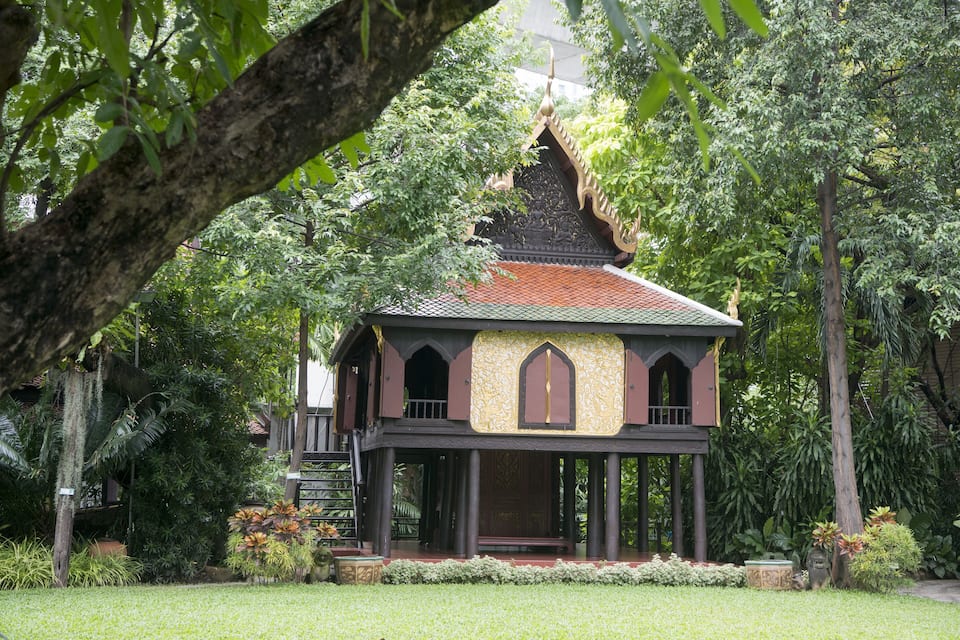 A traditional wooden house with a tiled roof surrounded by lush greenery.