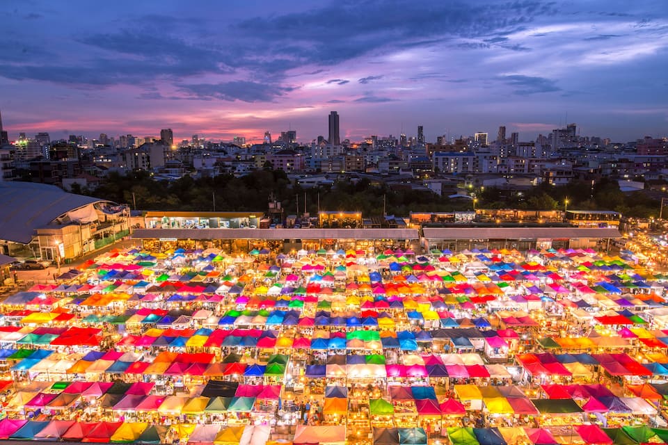 A vibrant night market with colorful umbrellas and stalls under a city skyline.