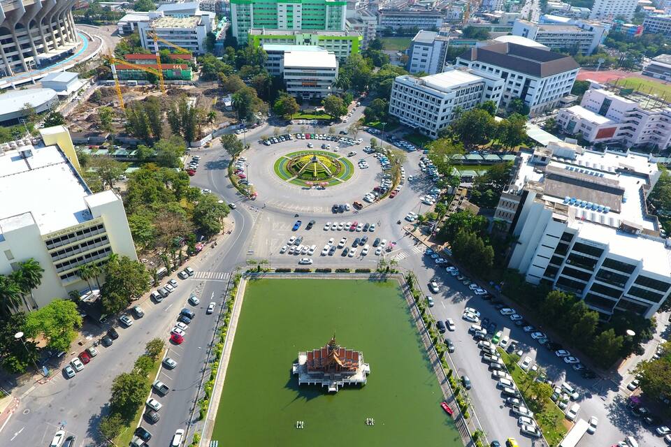An aerial view of a city with a central roundabout, surrounding buildings, and a large green park with a fountain.