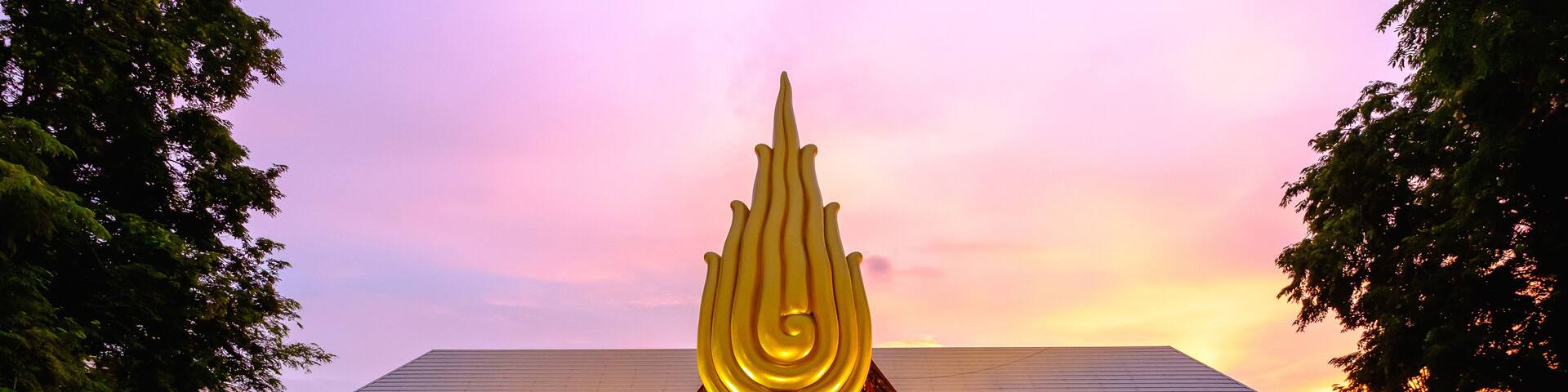 A large golden sculpture in front of a modern building with a unique roof design.