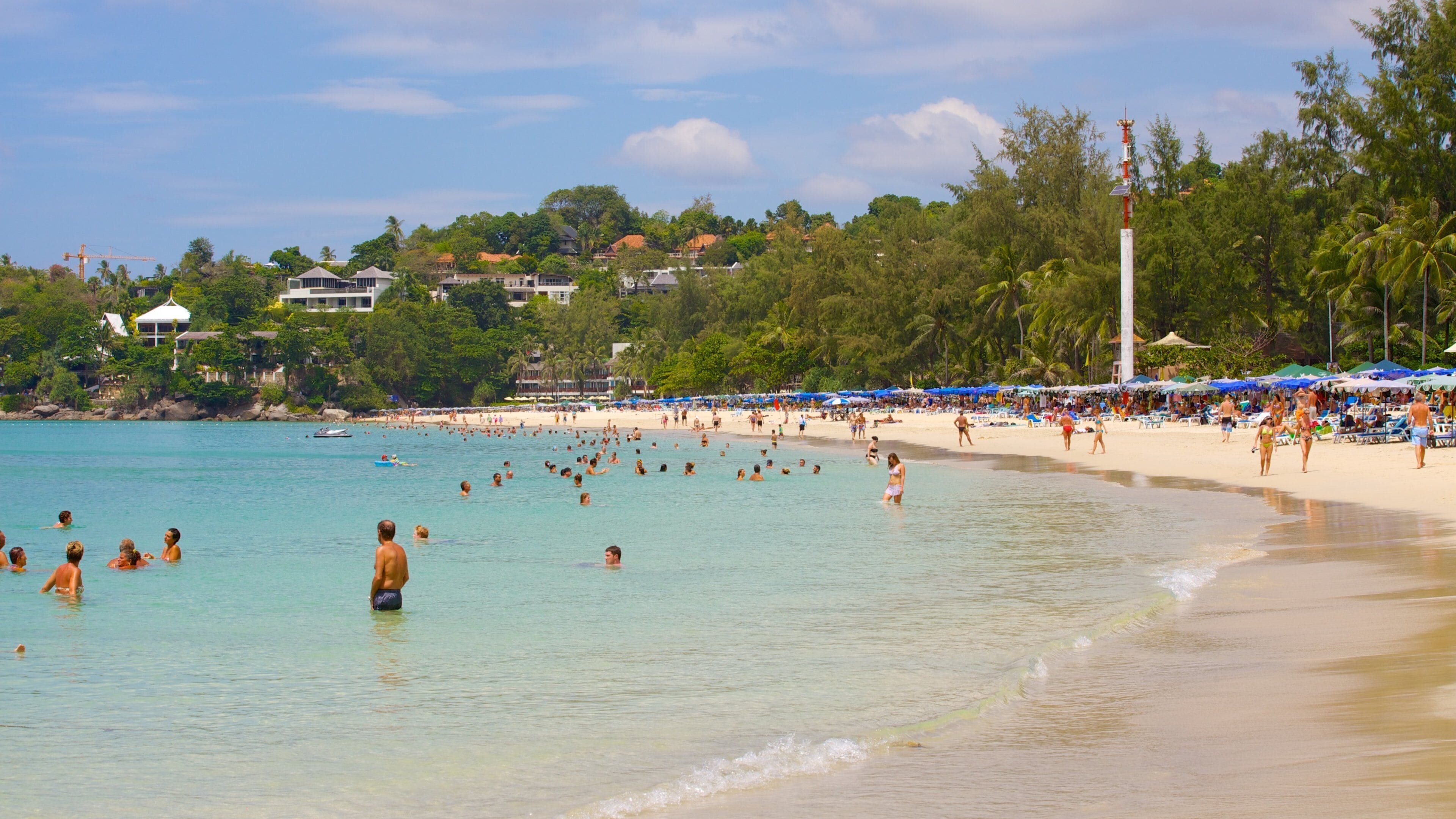 Une plage animée, avec une eau turquoise et limpide, des palmiers et des parasols de plage.