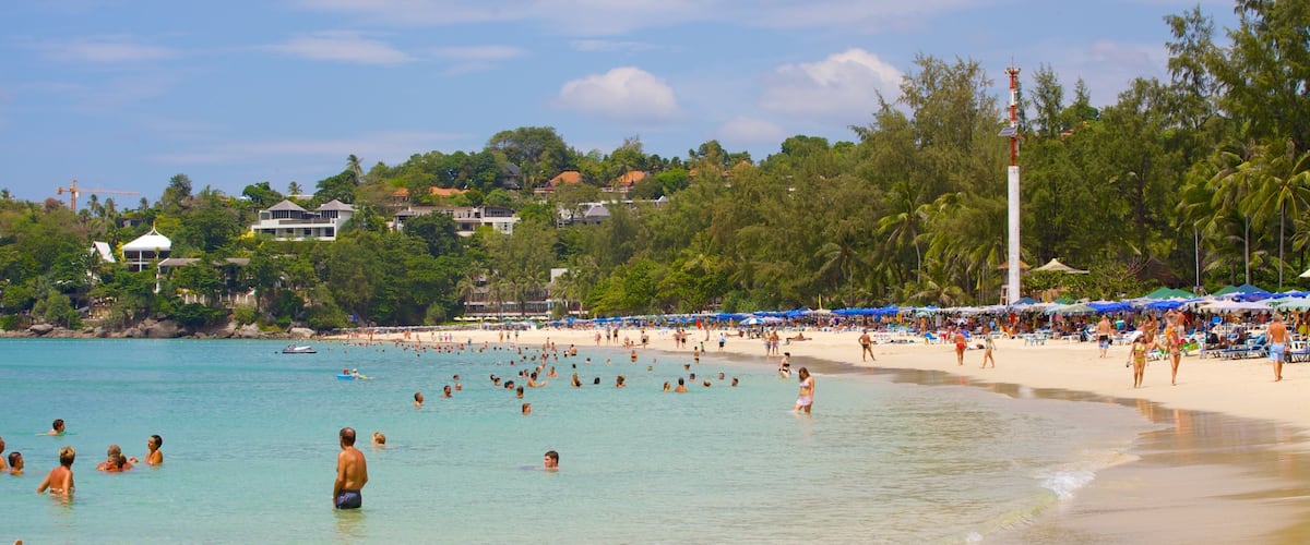A crowded beach with clear turquoise water, palm trees, and beach umbrellas.