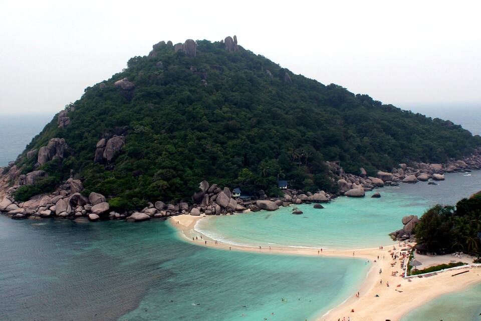 A tropical island with a beach, surrounded by clear turquoise waters and lush greenery.