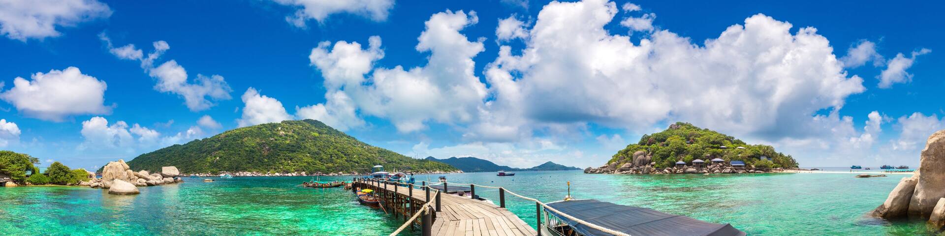 A pier extending into turquoise waters, surrounded by lush green islands and clear blue skies.