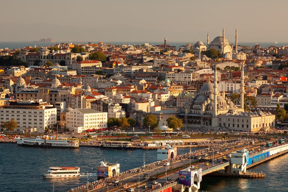 A cityscape with a prominent mosque with two minarets, a waterfront promenade, and a large body of water.