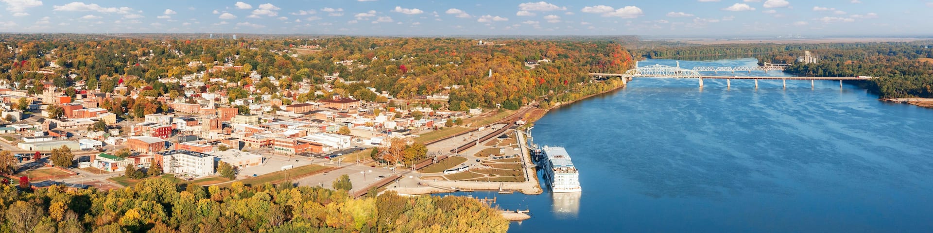 A river with a bridge, a town with buildings, and autumn-colored trees.