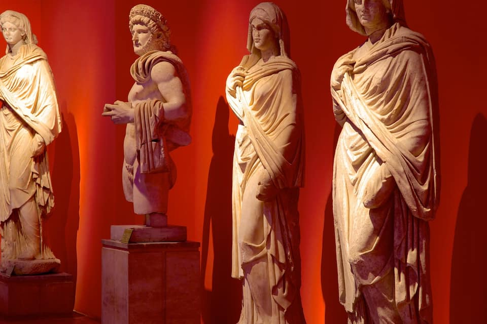Trois statues classiques en marbre, sur un fond rouge.