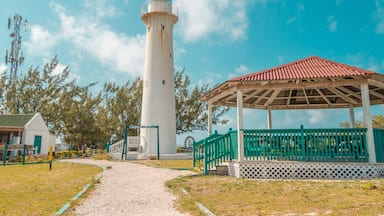 Un faro blanco con techo rojo, un porche de madera y un cielo azul despejado.