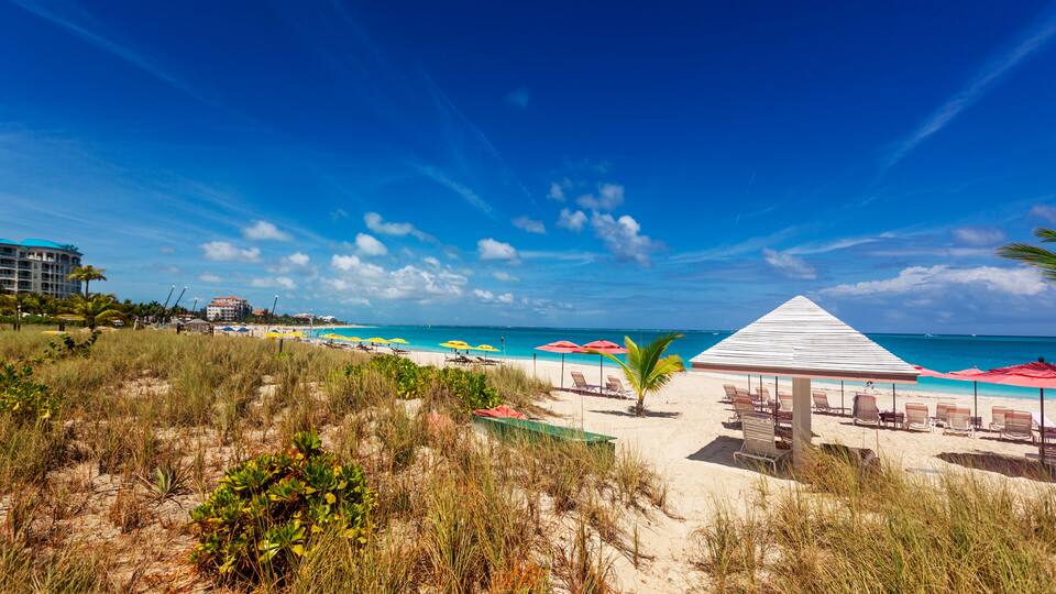 A beach with a white gazebo, red umbrellas, and clear blue water.