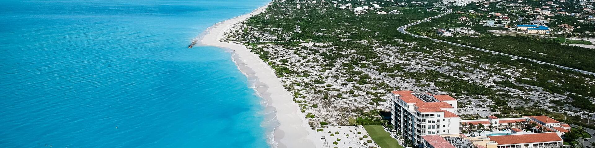 A coastal town with a beach, clear blue waters, and a large hotel complex.