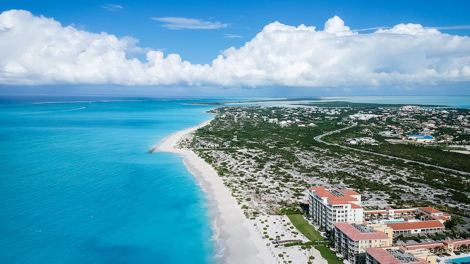 A coastal town with a beach, clear blue waters, and a large hotel complex.