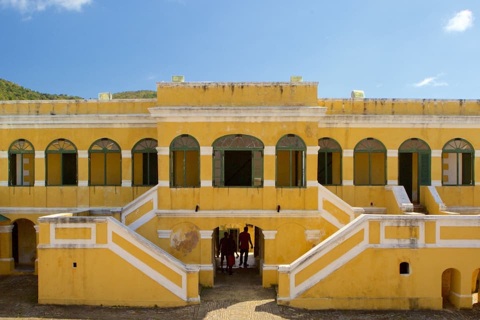 Um edifício de estilo colonial amarelo, com janelas em arco e uma escadaria central.