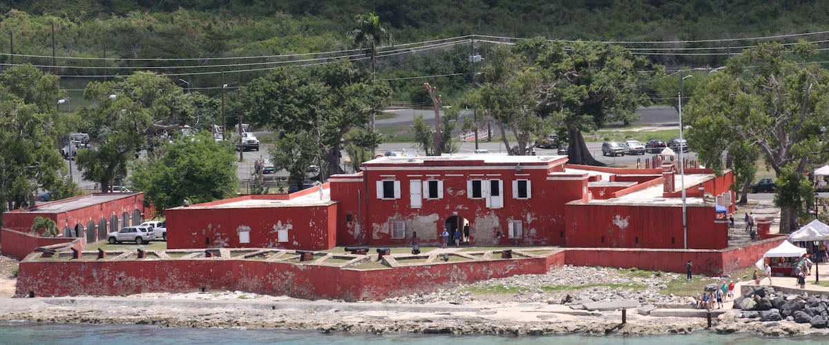 A coastal fort with red walls, a sandy beach, and a clear blue sea.